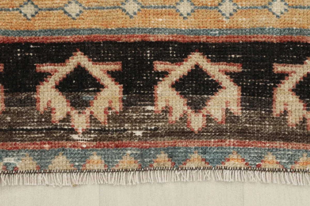 Close-up of the rug's border, featuring a black band with beige tribal designs and subtle fringe