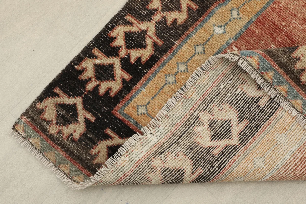 View of the rug folded to show the wool pile, cotton foundation, and intricate border detail