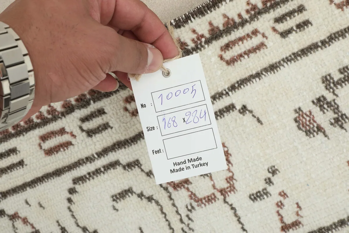 Hand holding a tag indicating the rug's dimensions and its hand-made origin in Turkey.