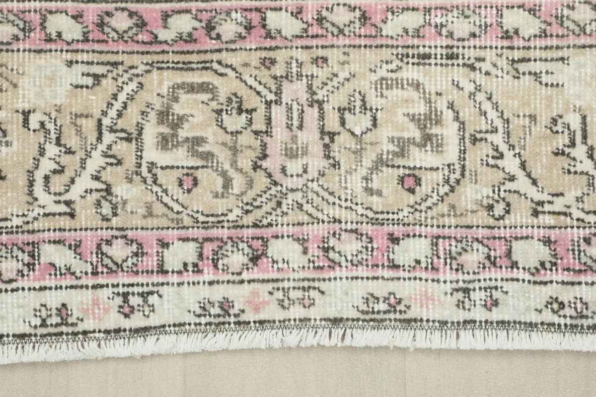 Detailed view of the rug's border pattern, showing pink and beige tones