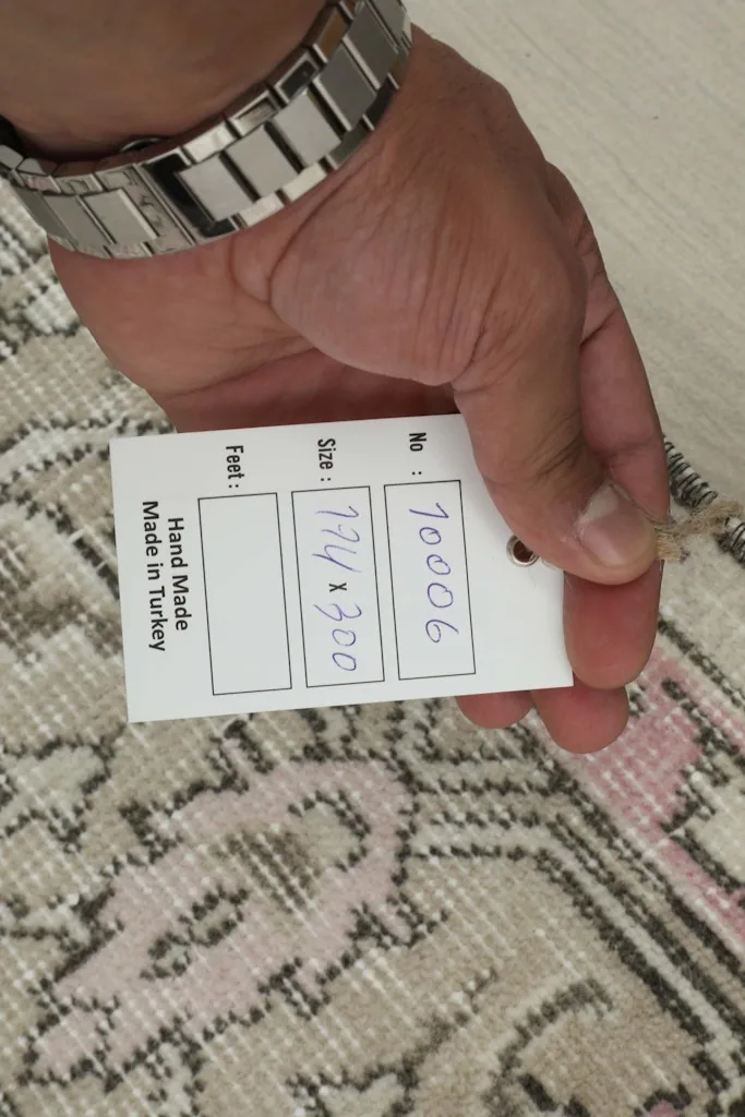 Hand holding a tag showing rug details including 'Hand Made in Turkey' and size