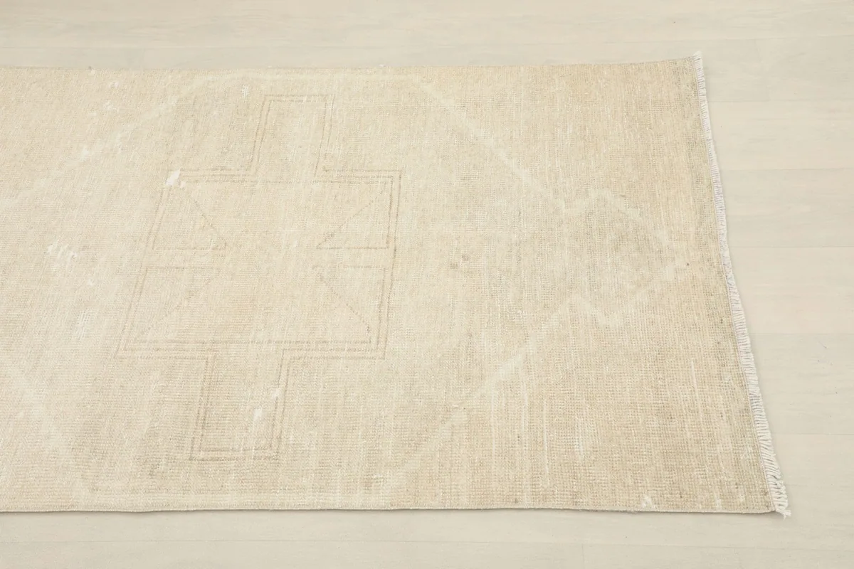 Detailed view of one end of the beige runner rug, showing subtle geometric patterns and texture.