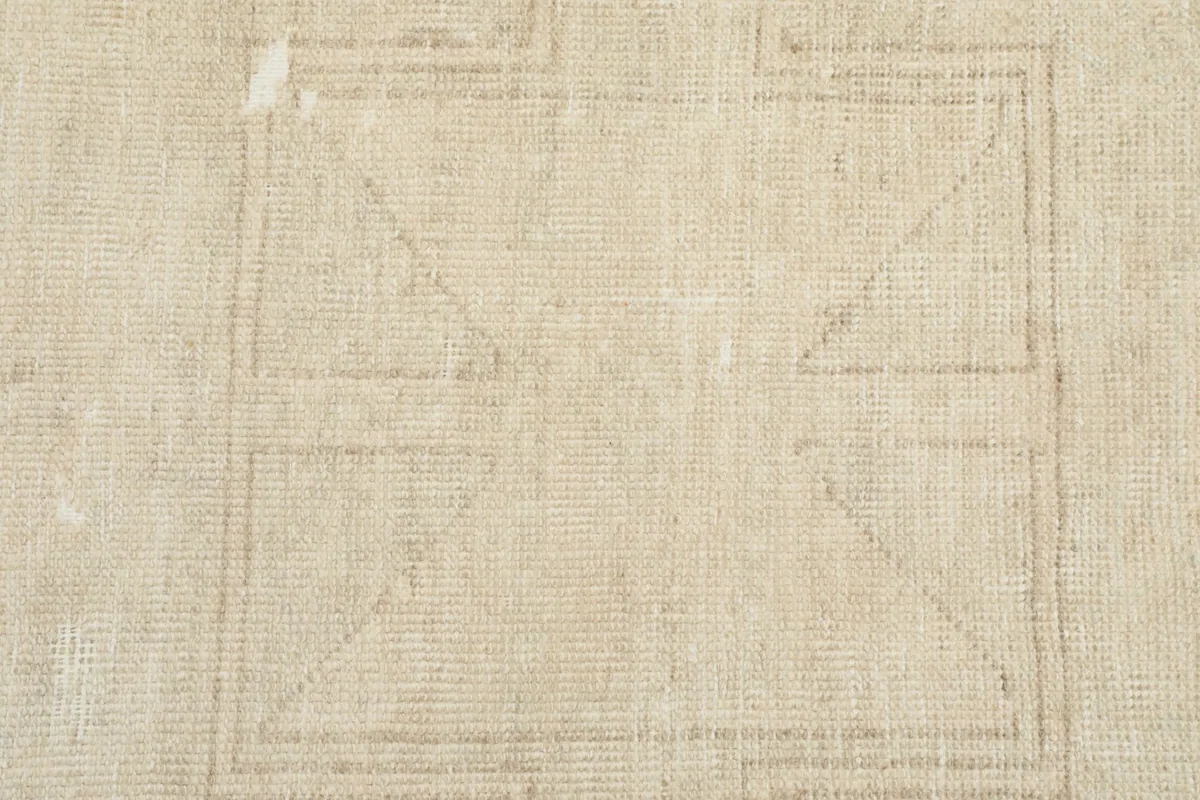 Tight close-up of the low wool pile and the hand-knotted texture of the beige vintage rug.