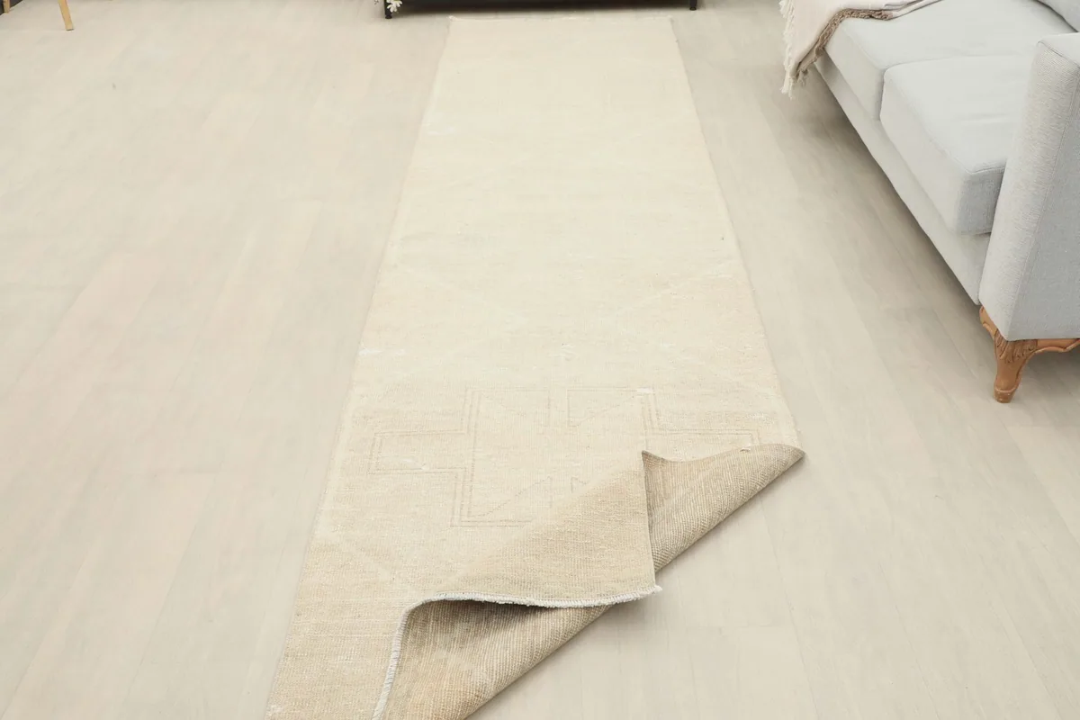 The beige runner rug partially folded, showing the flexibility and thickness of the wool pile.