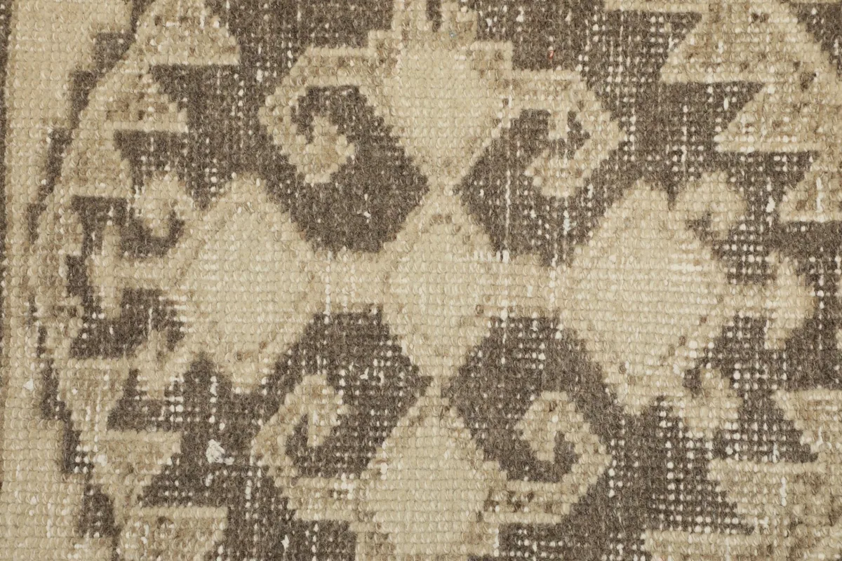 Close-up view of the low wool pile texture and the distressed appearance of the brown geometric pattern