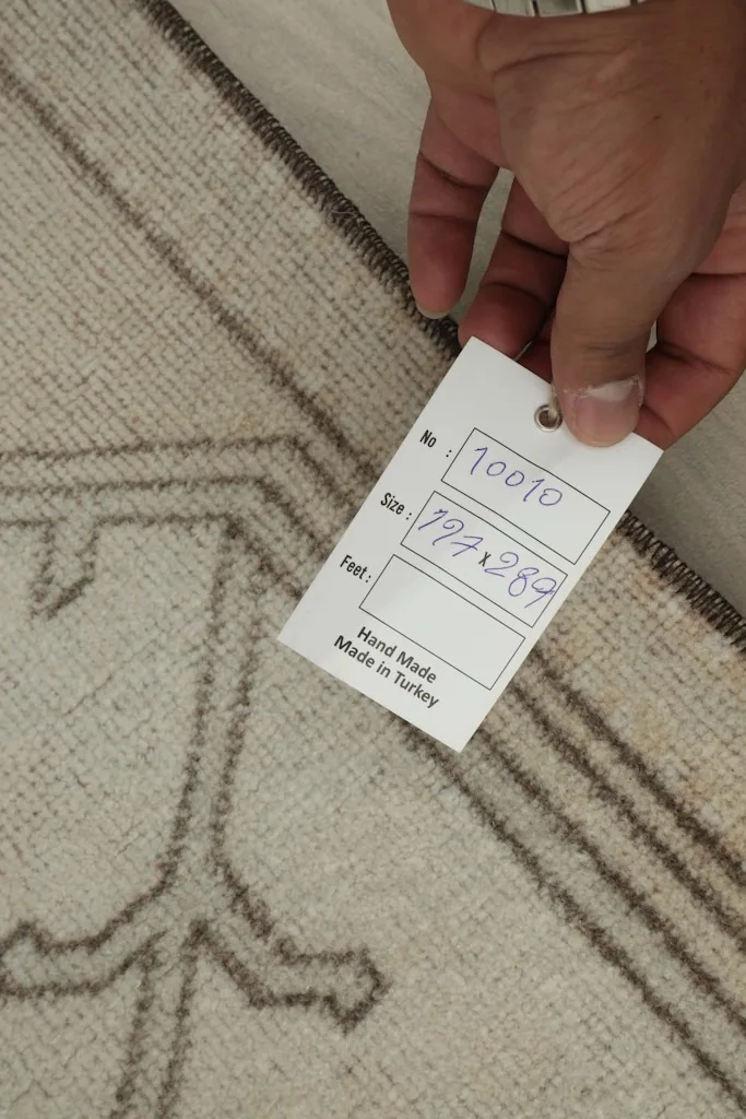 Hand holding a tag showing the rug's size in centimeters and its handmade origin in Turkey
