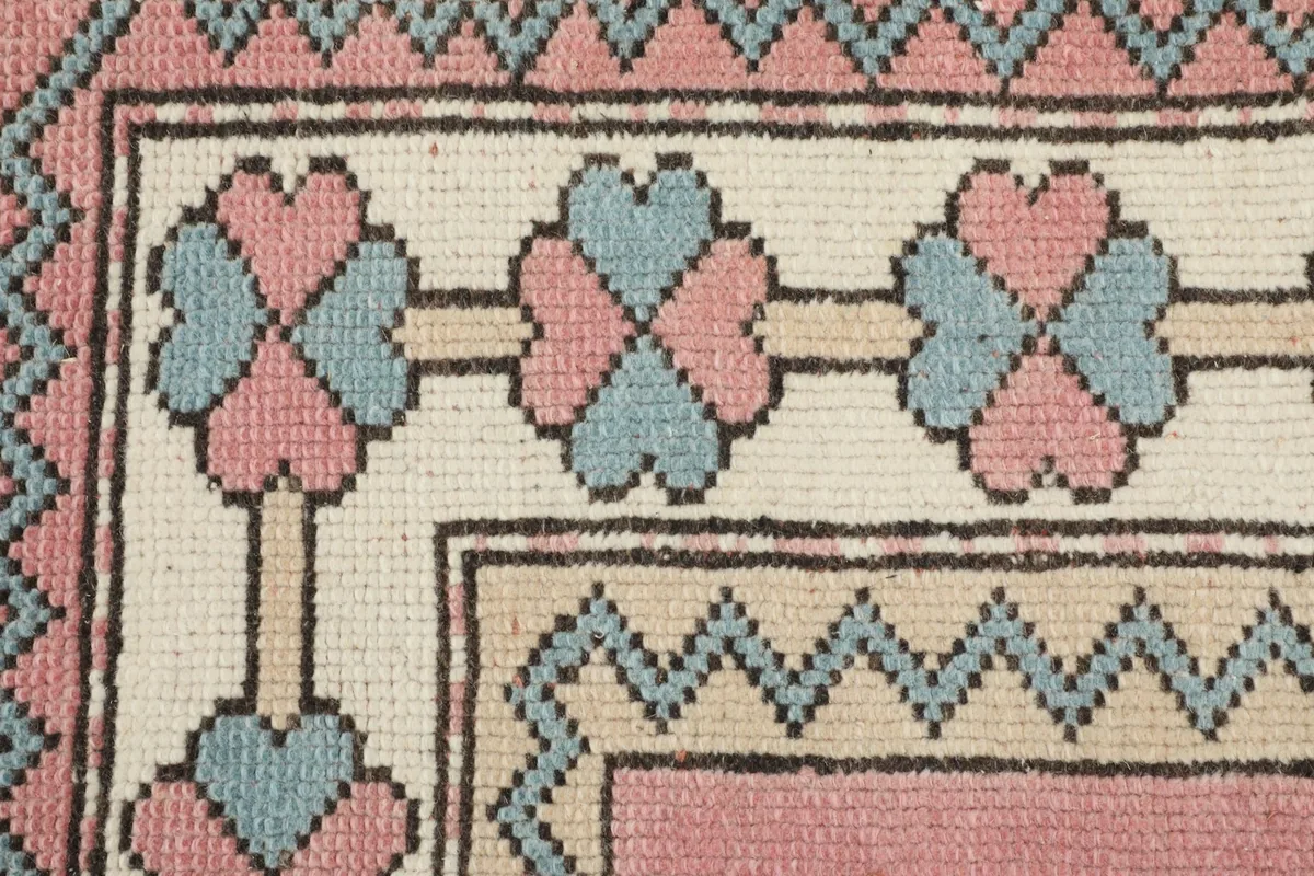 Close-up of the rug's border, featuring pink and blue clover-like motifs on a cream background