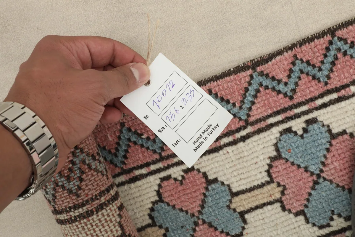 Hand holding a tag showing rug details including size 156x235 cm and handmade origin