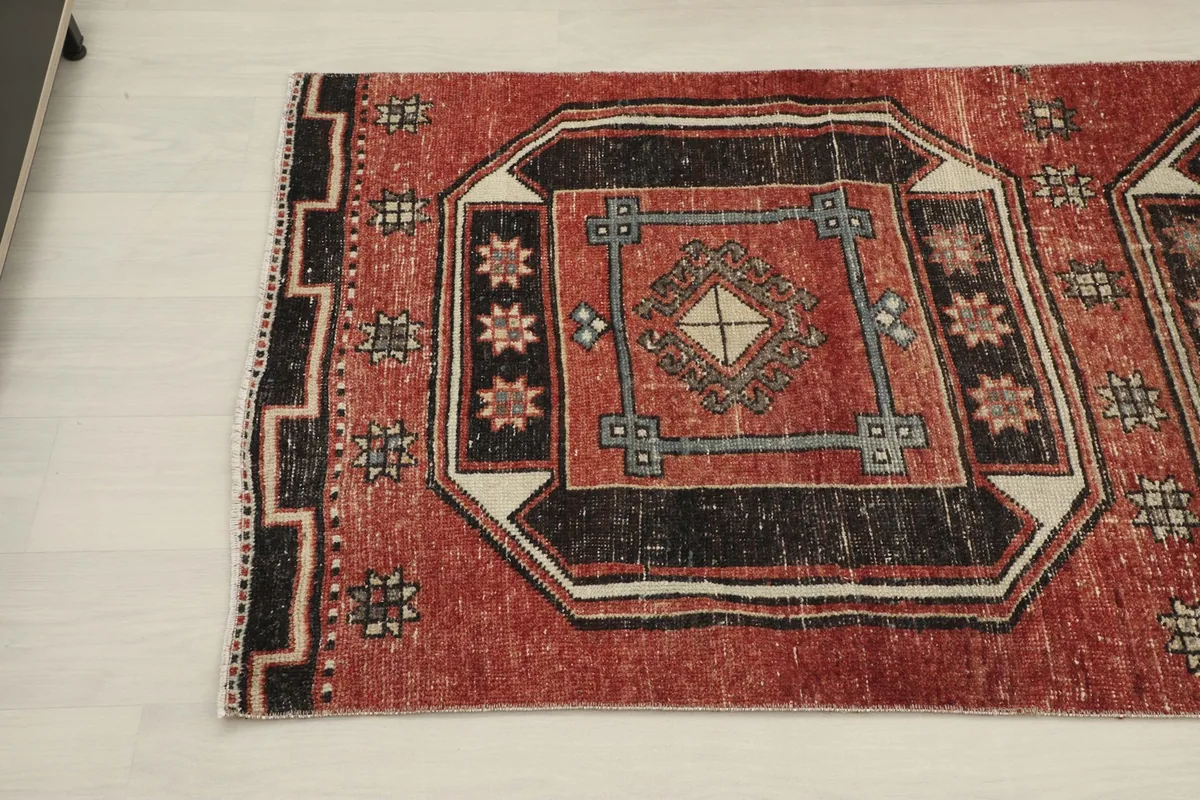 Angled view of the vintage runner rug's pattern and border, highlighting the black and rust colors.