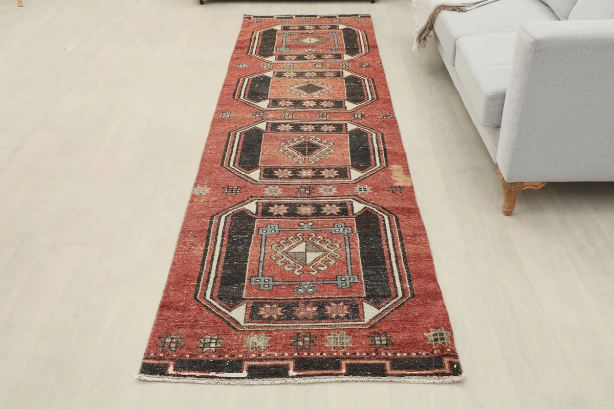 Full view of the vintage rust and black runner rug laid out in a room, next to a light gray sofa.