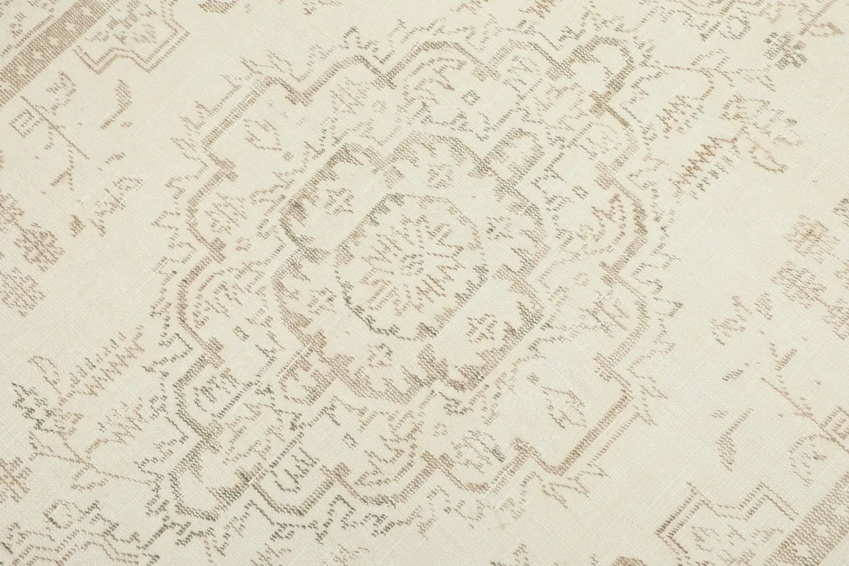 Macro detail of the central medallion design on the cream vintage rug, highlighting the faded wool pile.