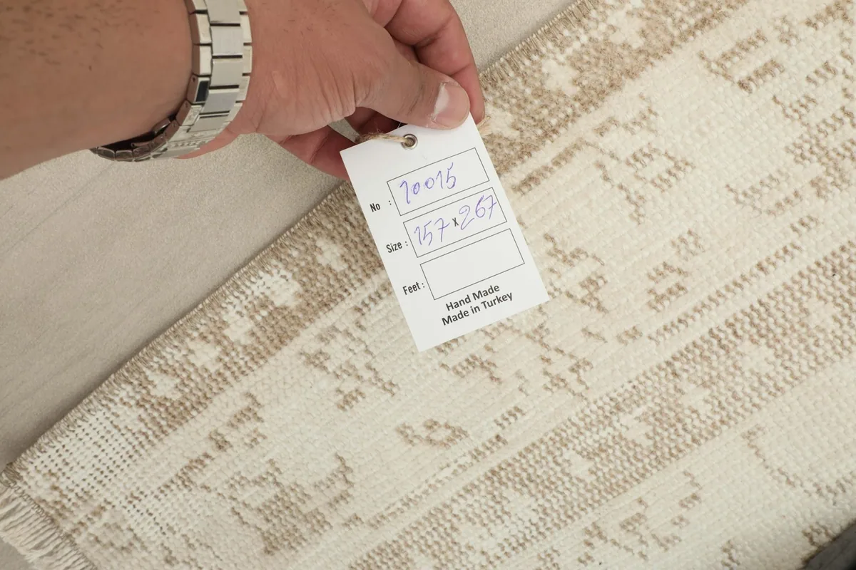Hand holding a tag showing the rug's dimensions and origin, with the rug's back visible.