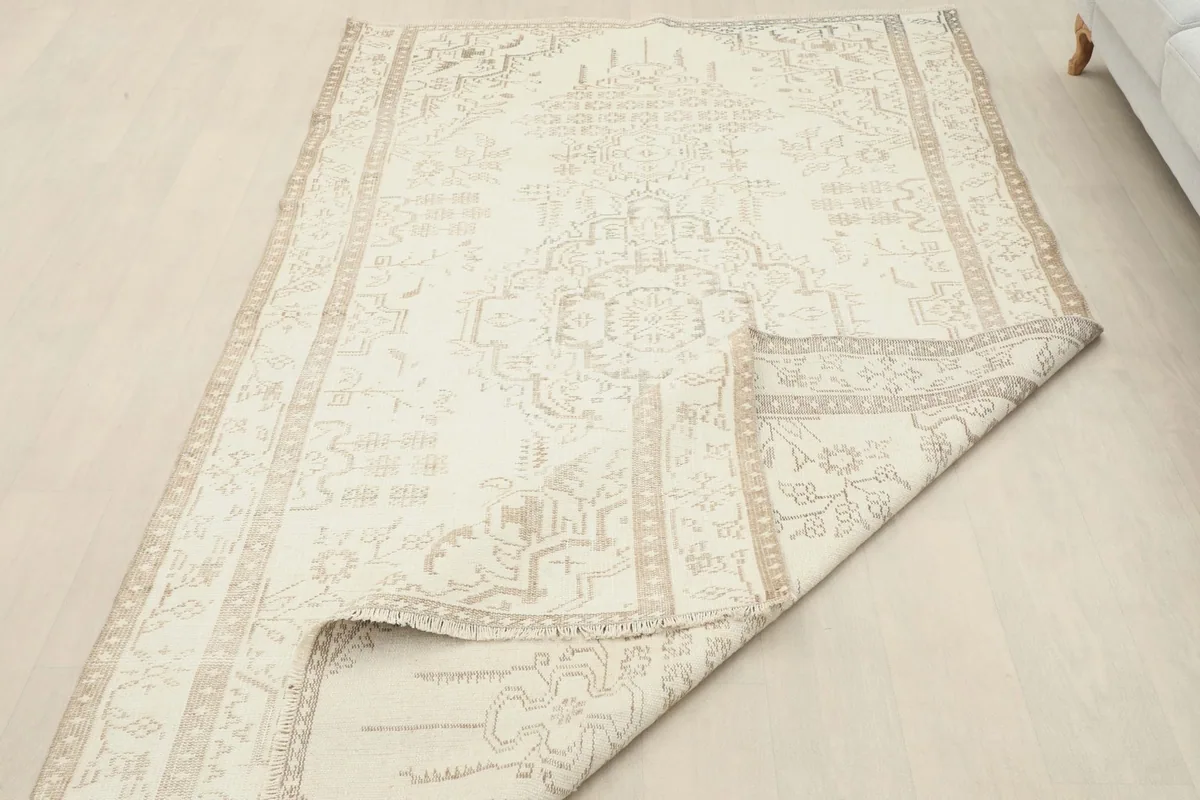 The cream and tan rug partially folded, displaying the back of the rug and the fringes.