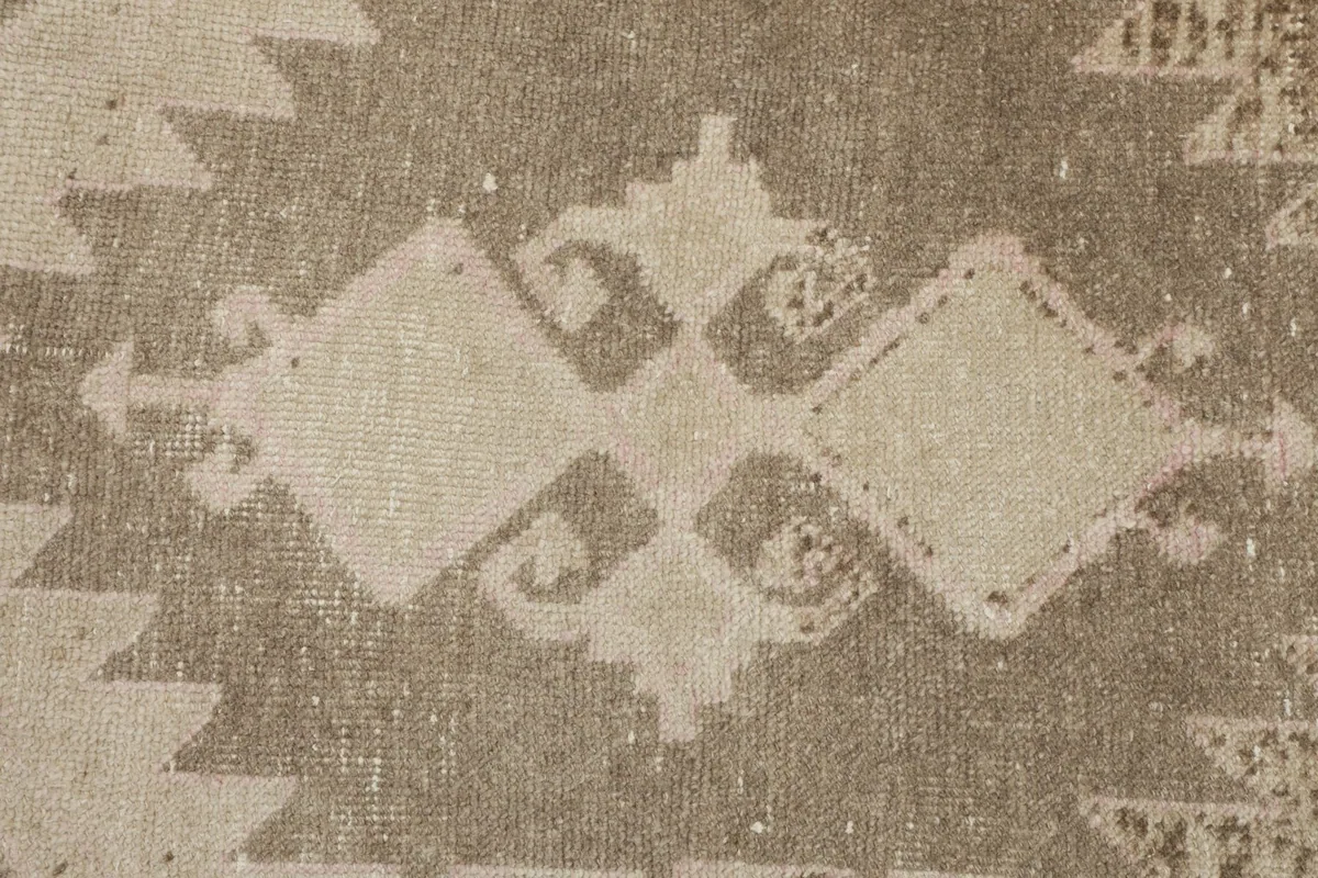 Extreme close-up of the beige and brown geometric design, revealing the hand-knotted wool pile and color variations.