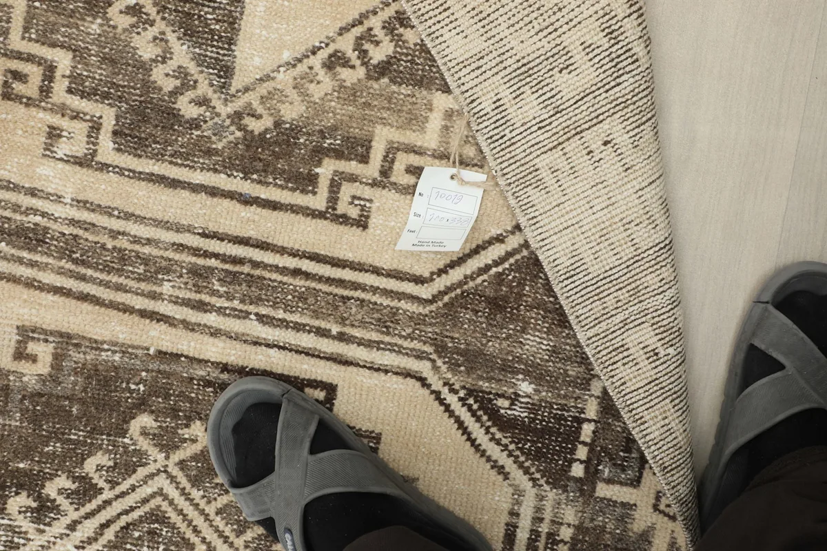 A person's feet in sandals next to the runner rug, with a tag visible on the folded corner.