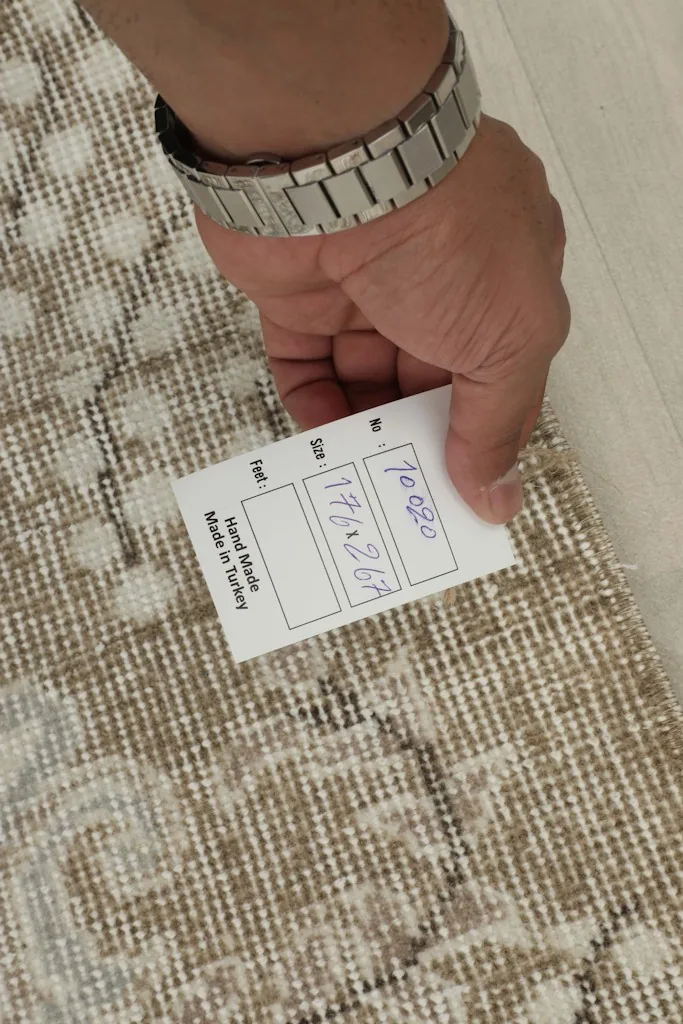 Hand holding a tag showing the rug's size and 'Hand Made in Turkey' against the rug's back