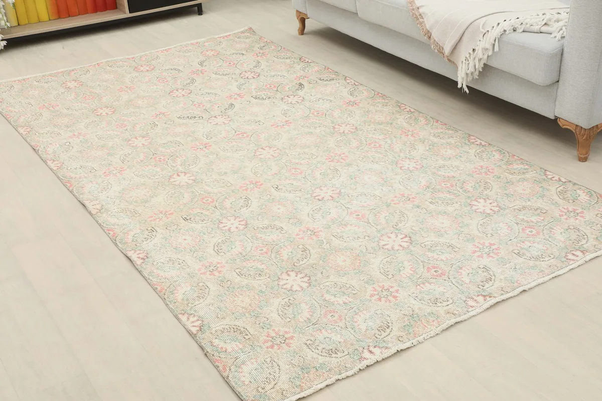 Vintage Anatolian rug with beige, pink, and green floral patterns placed in a room setting.