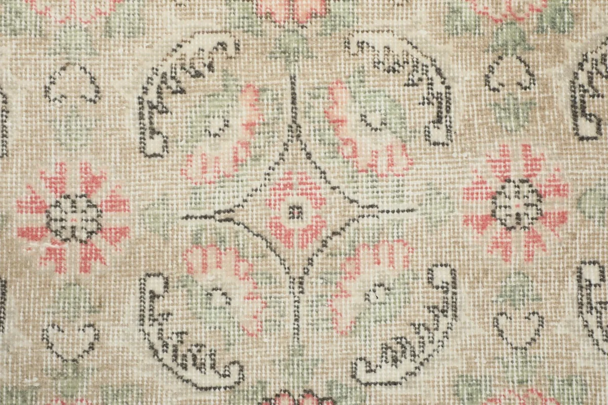 Detailed view of the rug's hand-knotted wool pile and the faded colors of its floral design.