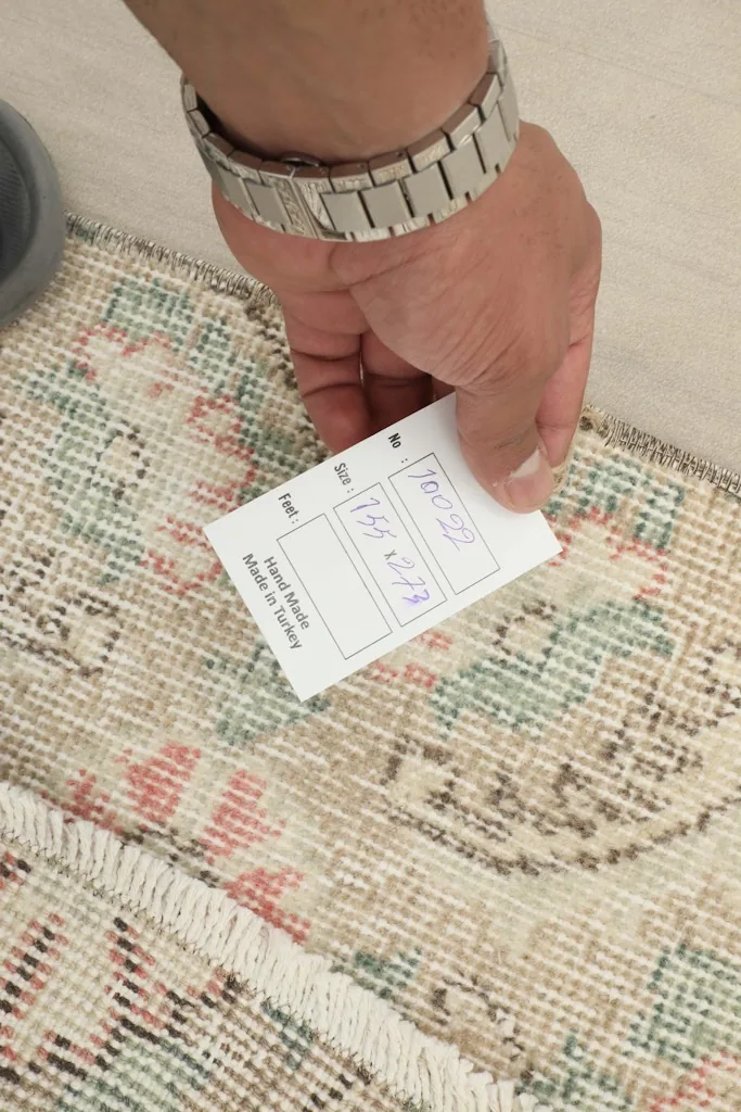 A hand holding a size tag (155 x 273 cm) next to the edge of the vintage Anatolian rug.