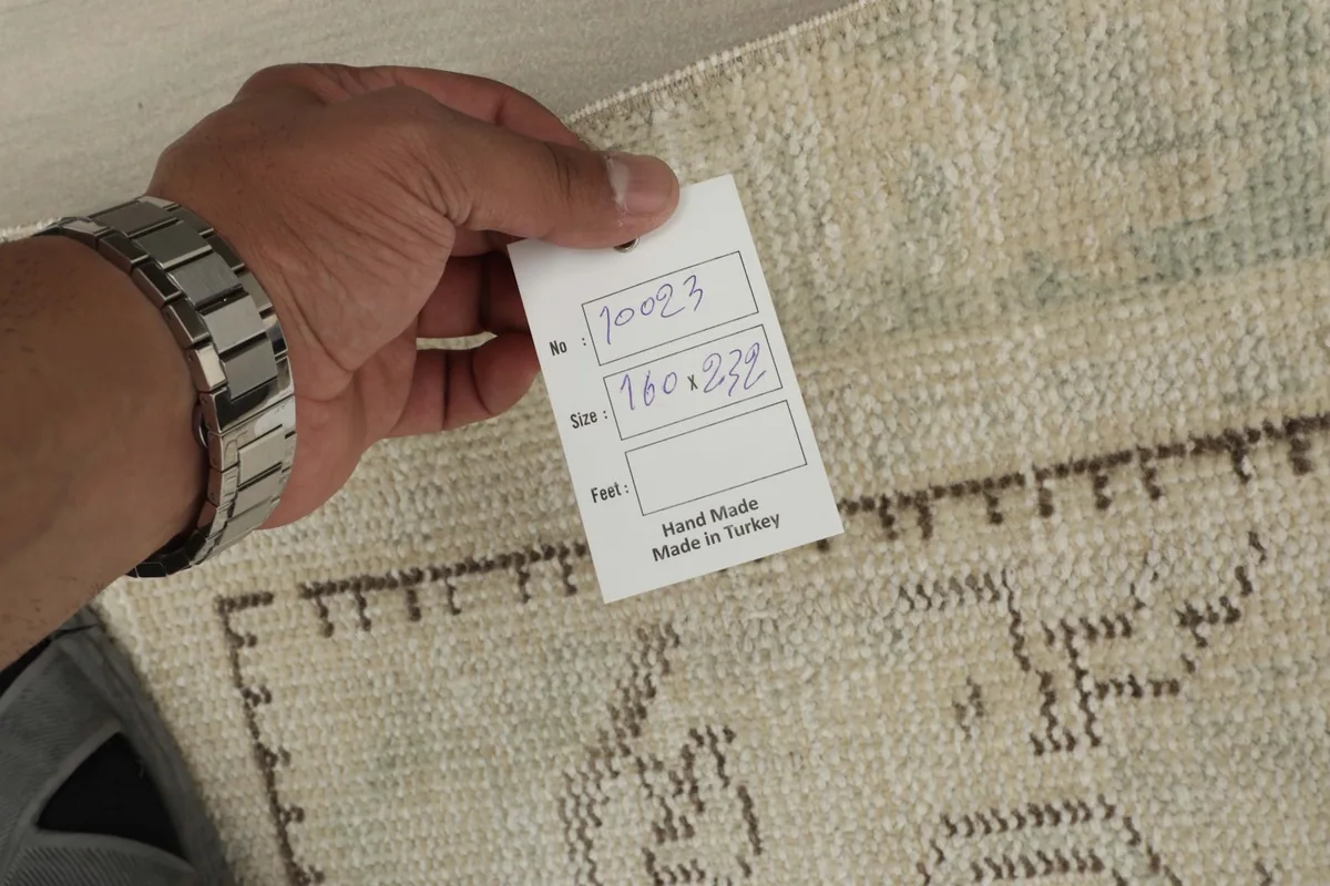 Hand holding a tag showing the rug's item number and dimensions (160x232 cm)