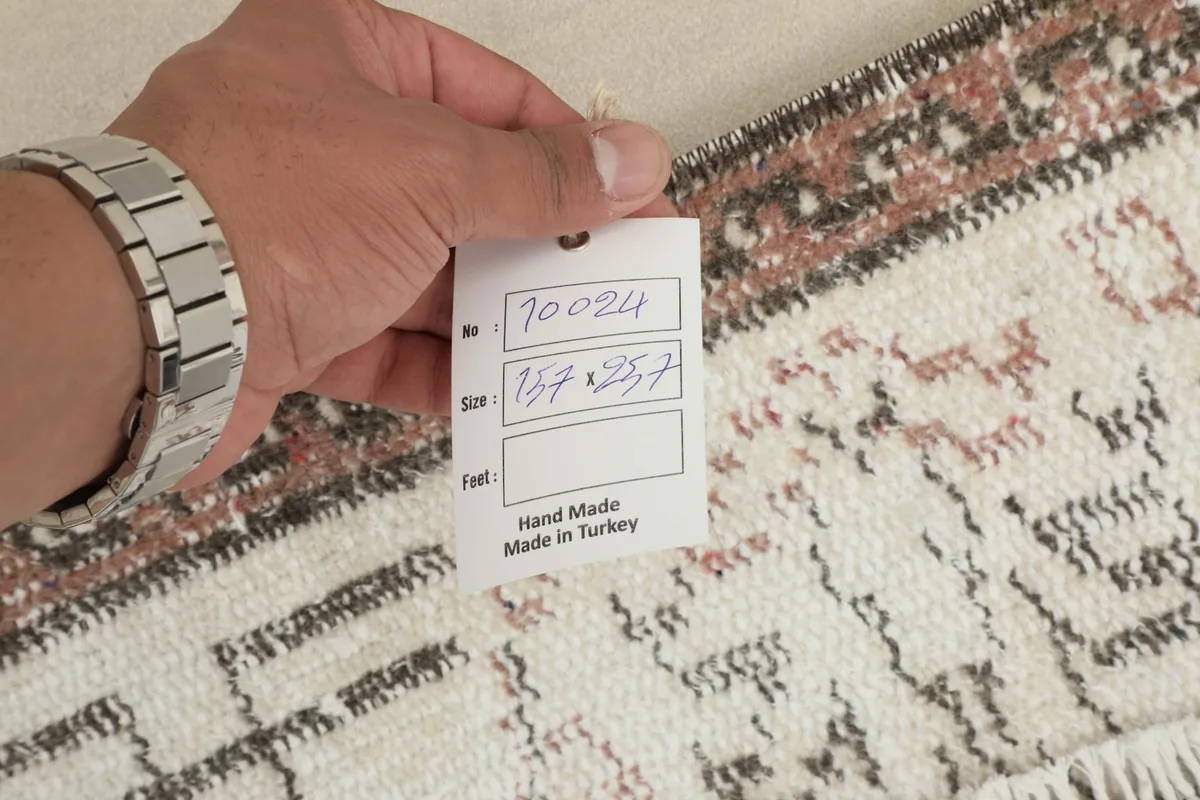 Hand holding a tag showing the rug's dimensions in centimeters and 'Hand Made in Turkey'