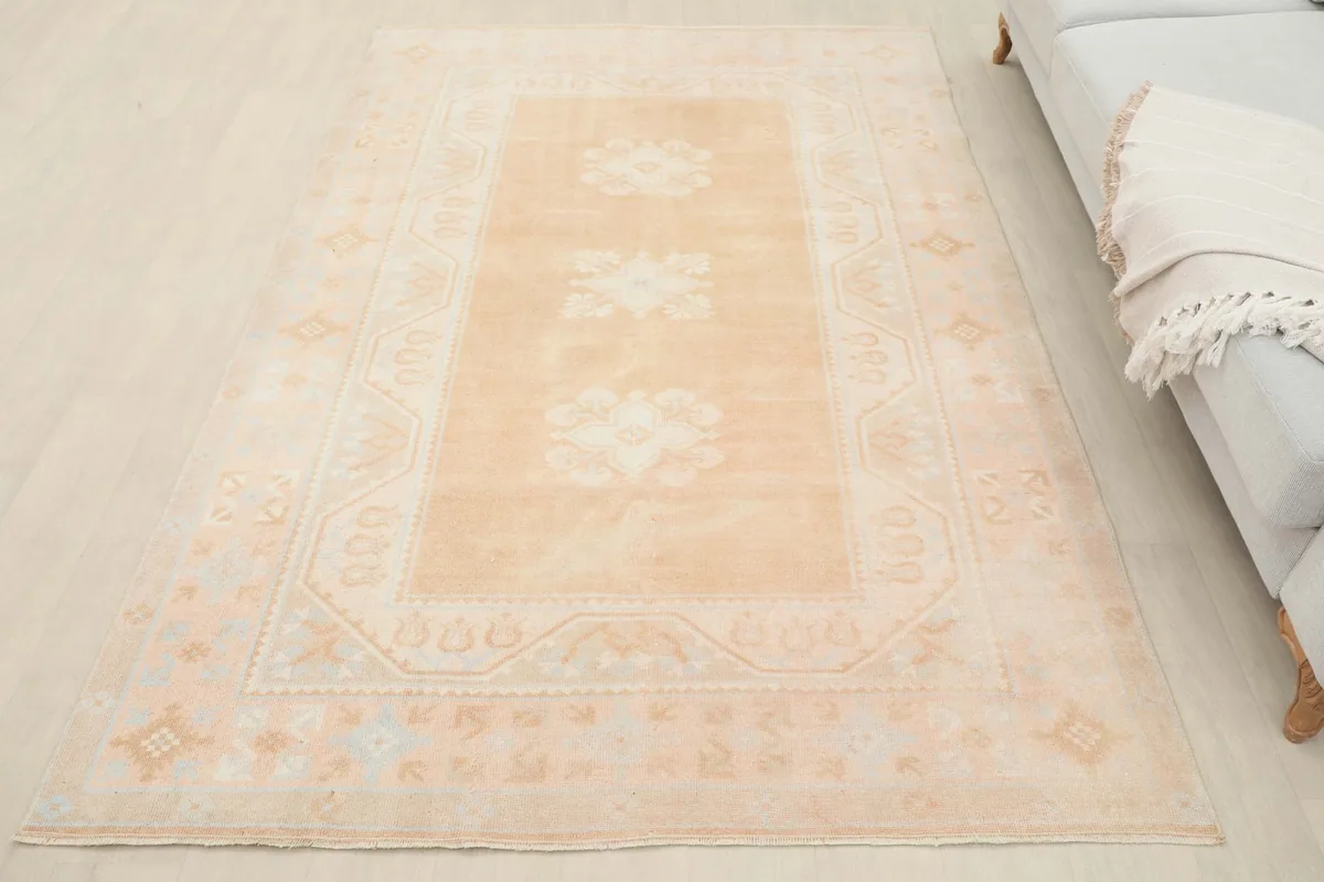 Full view of the beige floral geometric rug in a room, next to a light gray sofa