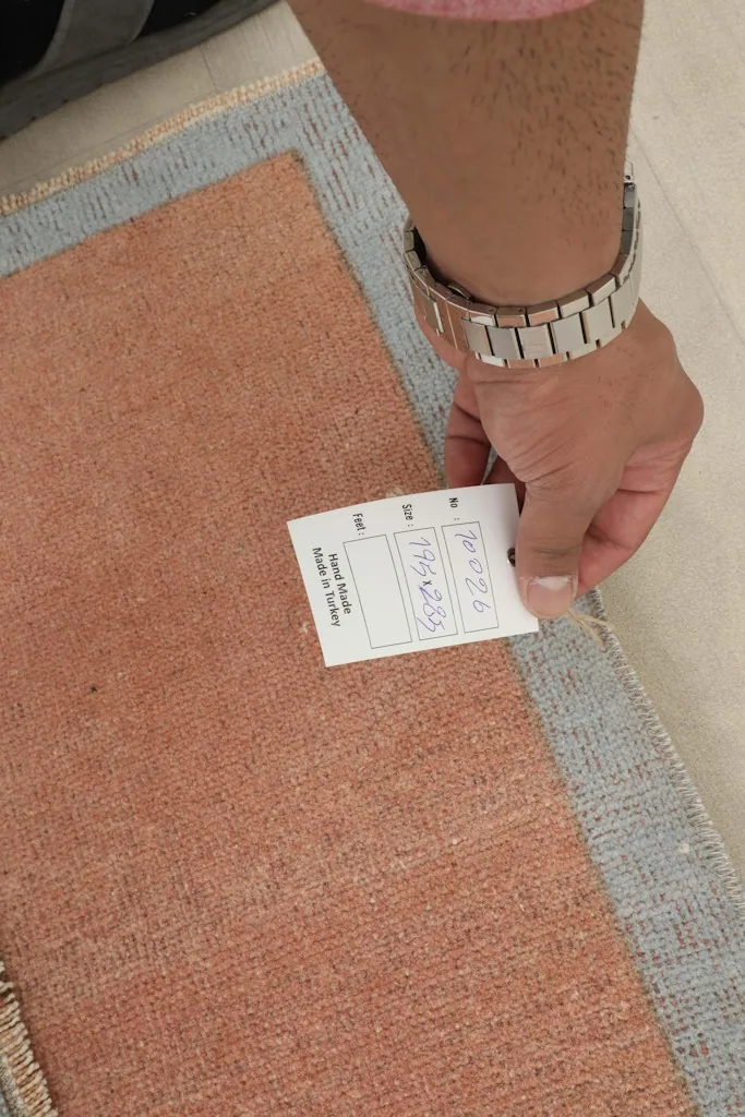 Hand holding a product tag near the rug, showing the texture of the rust field