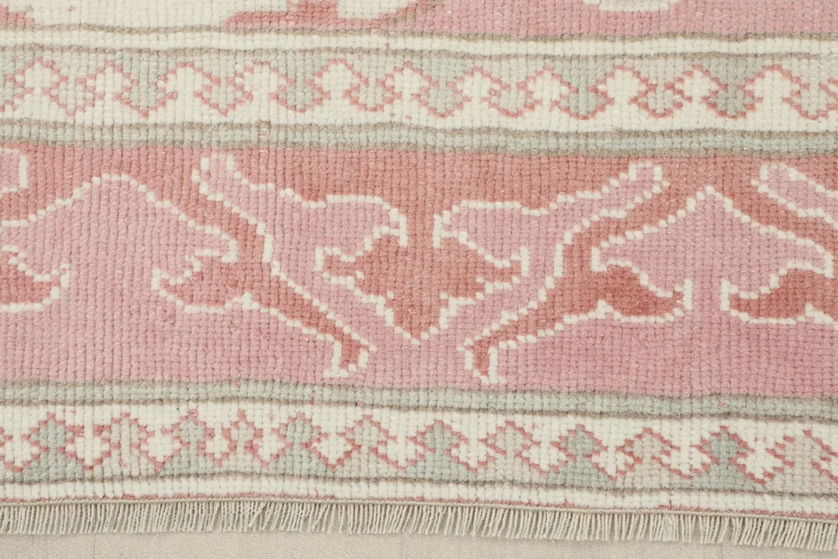 Close-up of the rug's border design, featuring rose, beige, and gray patterns and fringe.