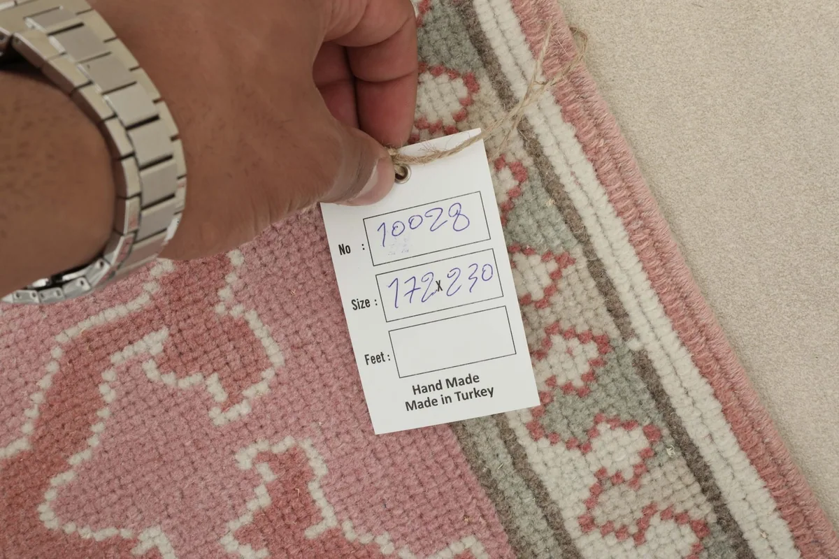 Hand holding a tag showing the rug's unique number and dimensions, confirming its handmade origin.