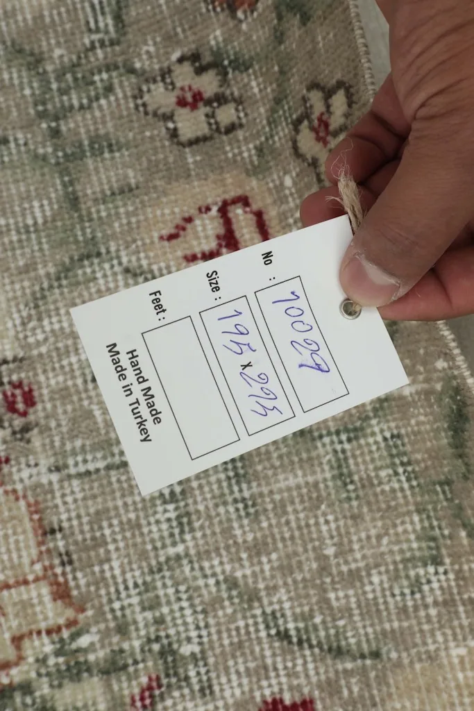 Hand holding a tag showing the rug's dimensions in centimeters, 195x295 cm