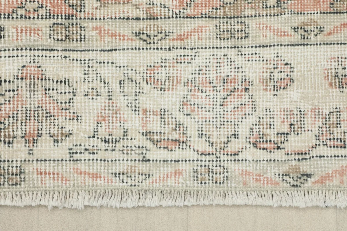 Detail of the rug's short, natural fringe and the intricate border design in ivory and tan