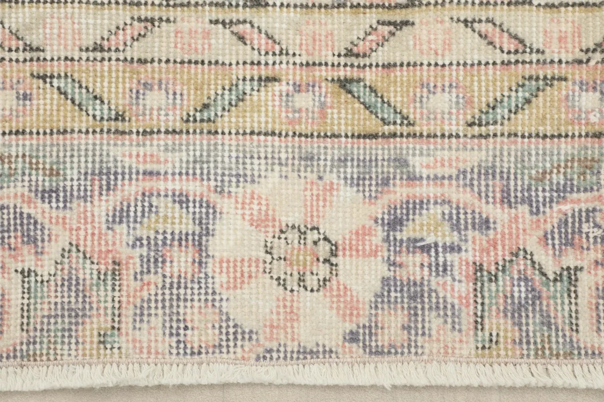 Detail of the rug's border, showing the blend of rose, blue, and tan colors.