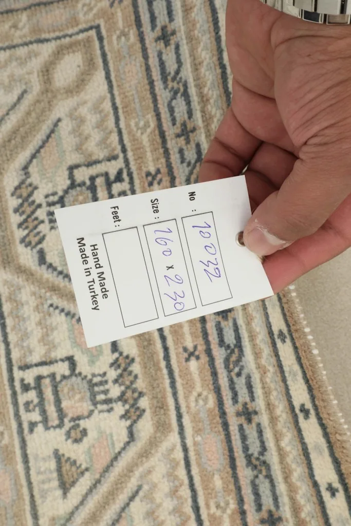 Hand holding a tag showing the rug's dimensions and origin, 'Hand Made in Turkey'