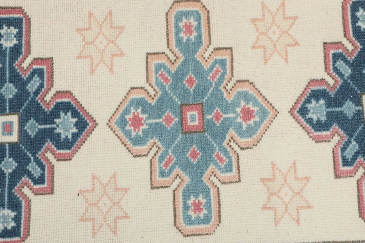 Detailed close-up of a central blue and rose geometric motif against the ivory background