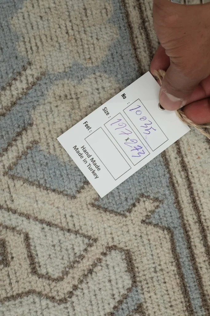Hand holding a tag showing the size and origin details of the vintage Anatolian rug