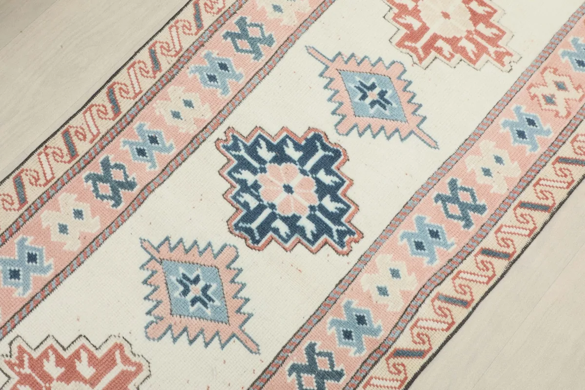 Close-up detail of the geometric patterns in ivory, rose, and blue on the runner's field.
