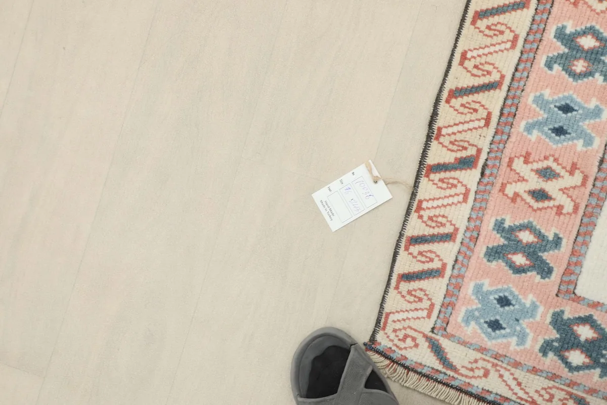 Corner of the rug with a size tag next to a foot, providing scale and detail of the fringe.