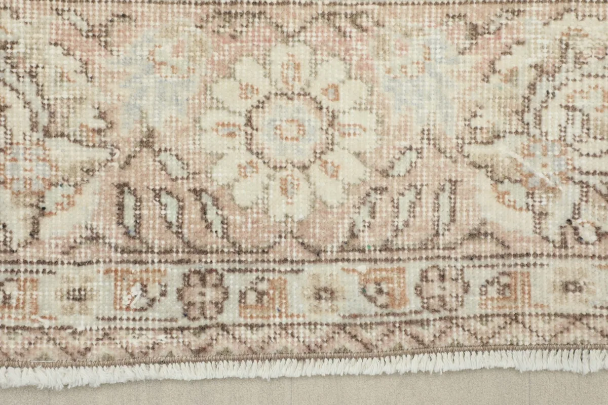 Detail of the rug's border, showcasing the beige and brown patterns and the fringe.