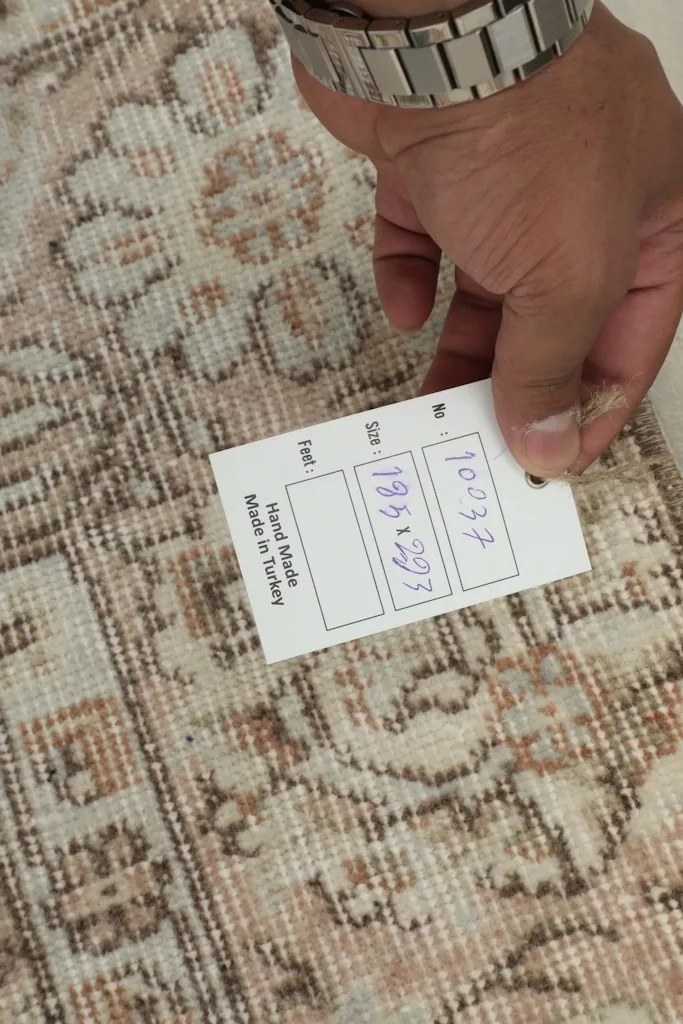 Hand holding a tag showing the rug's dimensions and origin, highlighting the hand-knotted quality.