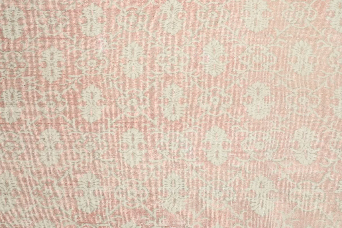 Close-up detail of the pink field and ivory floral motifs on the vintage rug