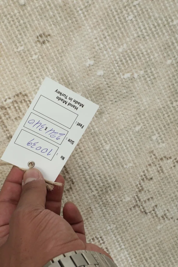 Hand holding a tag showing the rug's dimensions and origin over the rug's texture