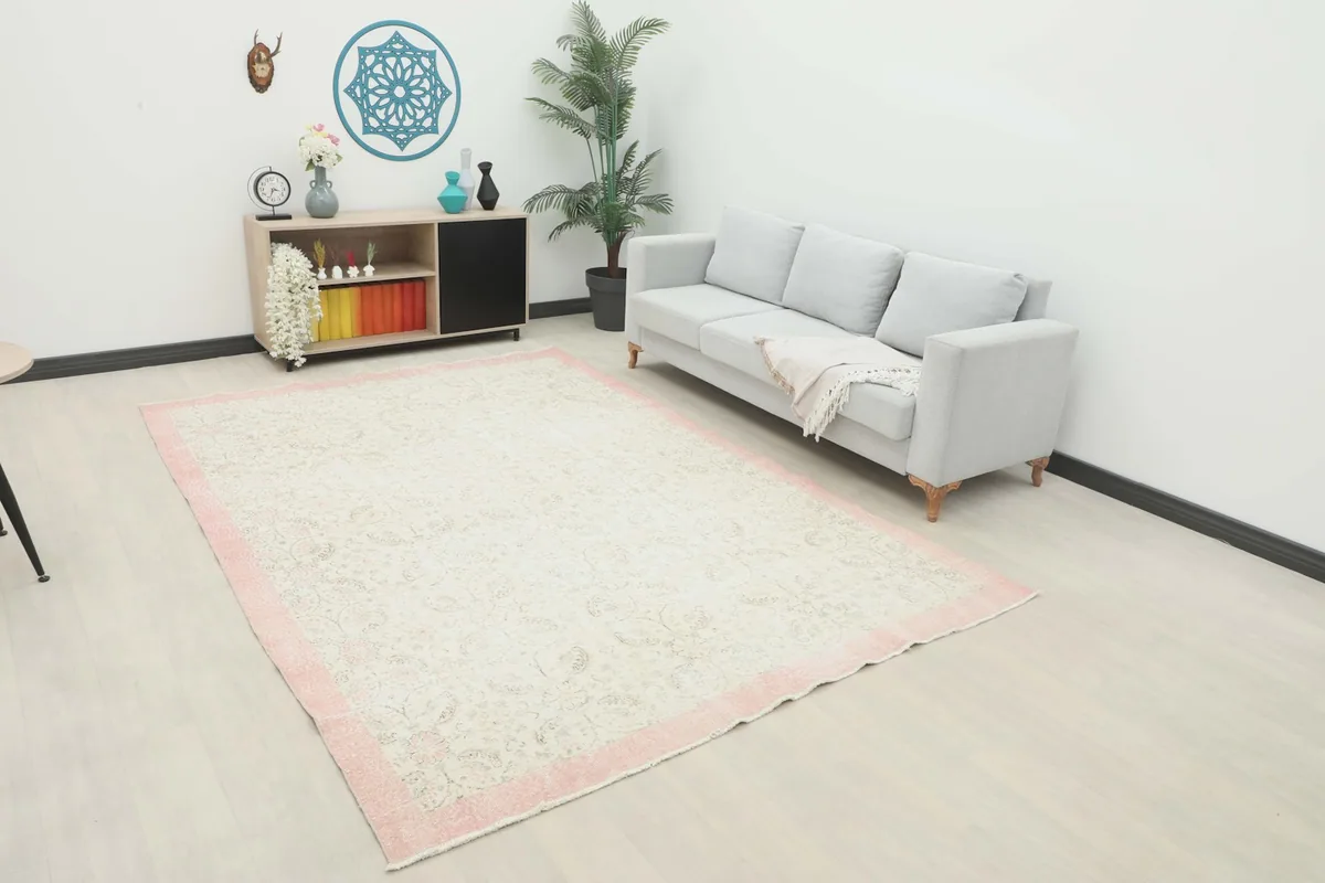 Large vintage ivory and rose rug displayed in a bright living room setting with a sofa and decor