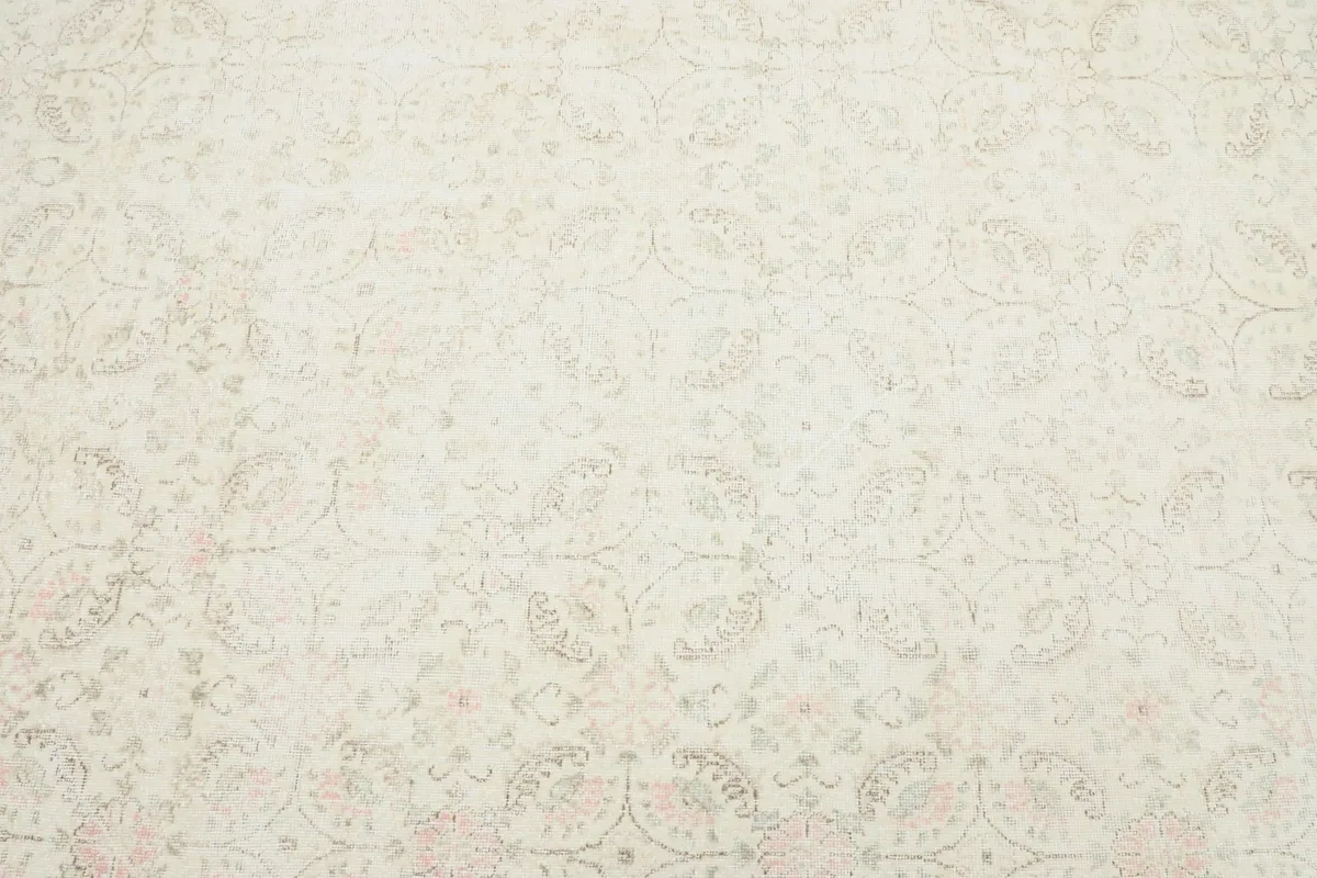 Close-up of the faded floral motifs and intricate details within the ivory field of the rug