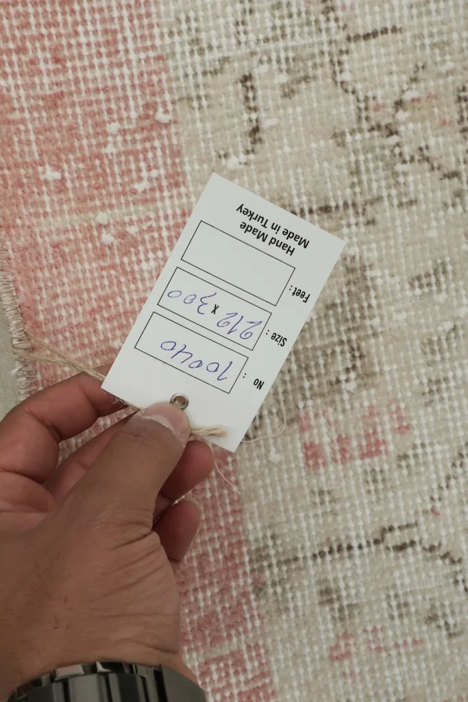 Hand holding a tag indicating 'Hand Made in Turkey' and rug dimensions over the rug's surface