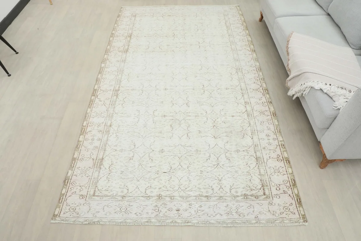 Full view of the ivory and beige vintage rug placed in a living room, viewed from a higher angle.