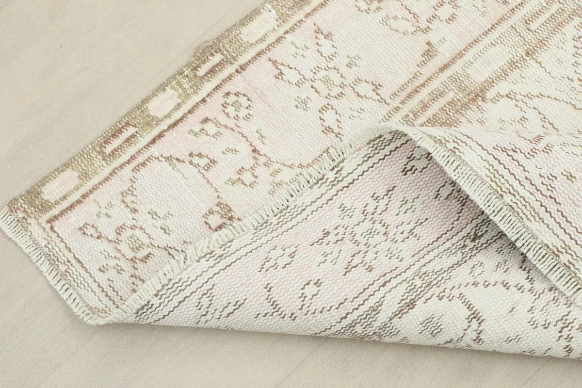 Corner of the rug folded back, showing the cotton foundation and the reverse side of the hand-knotted wool.