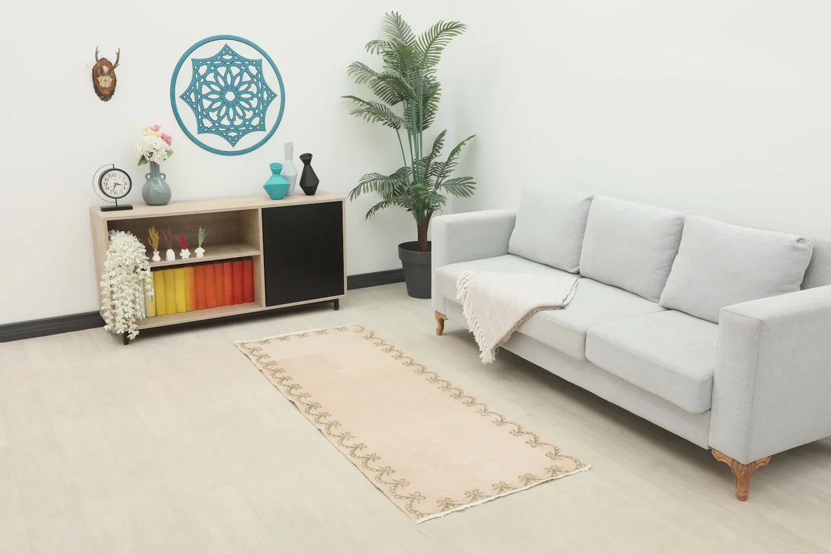 Beige and olive runner rug placed in a living room setting with a light gray sofa and wooden cabinet.
