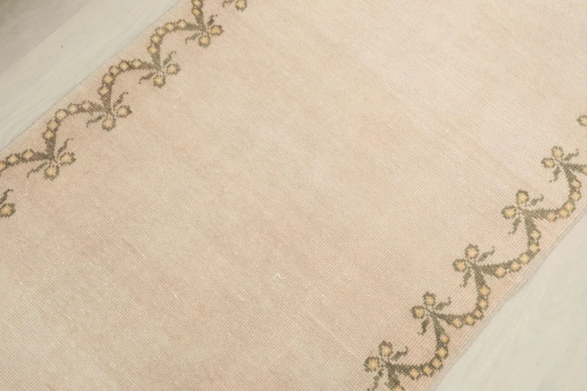 Detail view of the side border pattern of the beige runner rug with olive and gold geometric motifs.