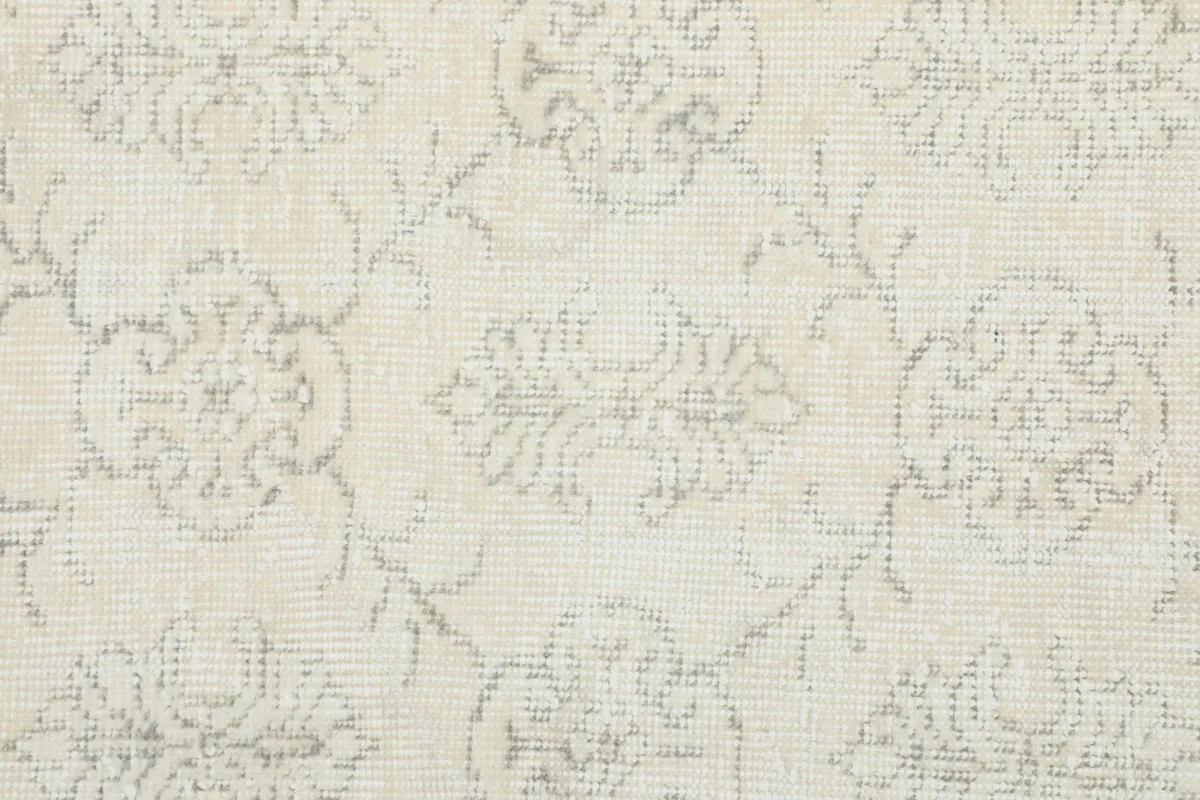 Detailed close-up of the hand-knotted wool pile and faded gray patterns on an ivory background