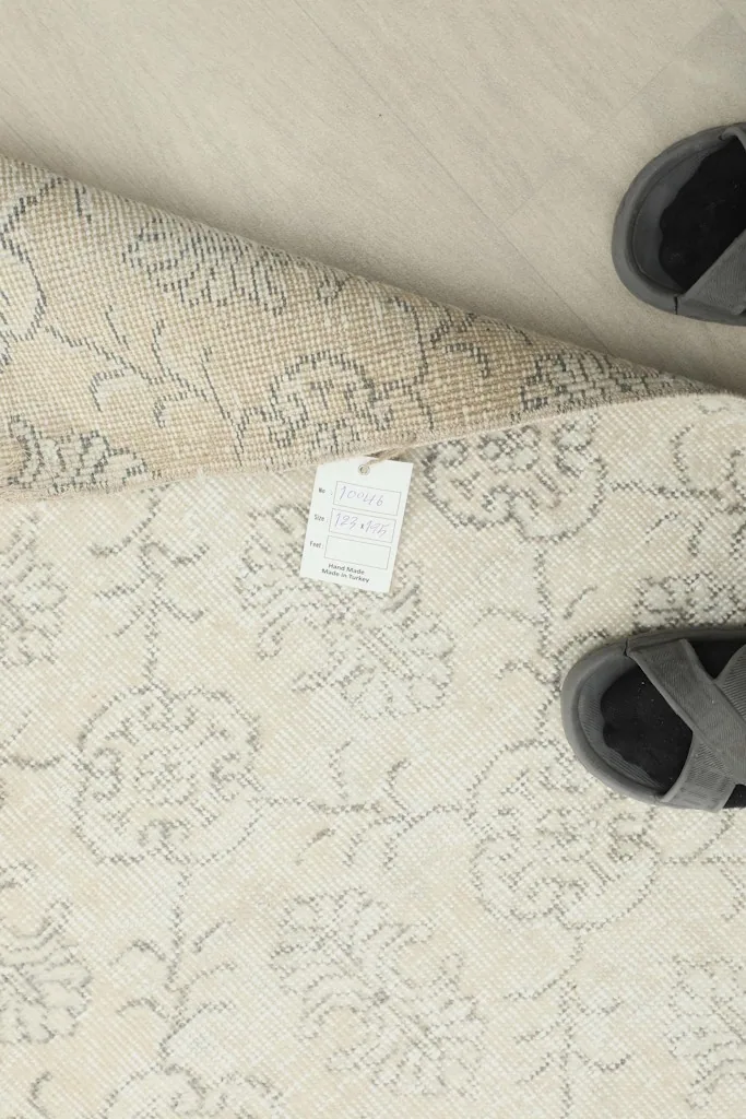 View of the rug's reverse side, showing the tag and hand-knotted details with sandals for scale